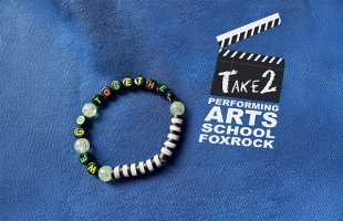 A beaded friendship bracelet with the words we go together spelled out lies on a blue background, with the Take2 performing arts school logo beside it