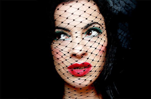 Camille O'Sullivan with heavy eye shadow and strong red lipstick - her face is half-covered by a black veil.