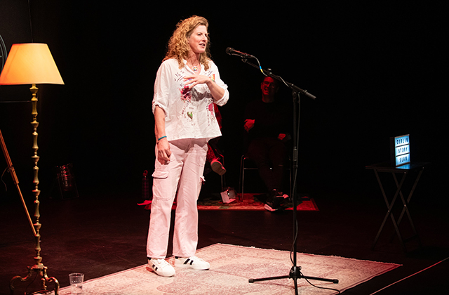 A woman with blonde curly hair wearing pink, telling a story on stage.