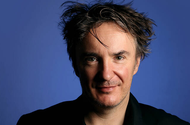 Headshot of Dylan Moran with a blue background