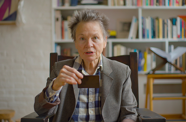 Laurie Anderson holding up a small black card.