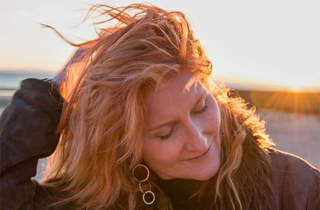 Eddi Reader outdoors with her eyes closed, the evening sun dramatically highlighting her windswept hair.