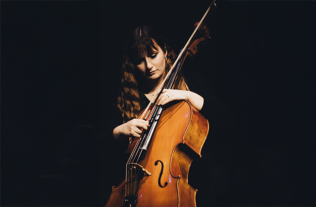 Dramatic shot of Flavia Massimo playing cello against a stark, black background.