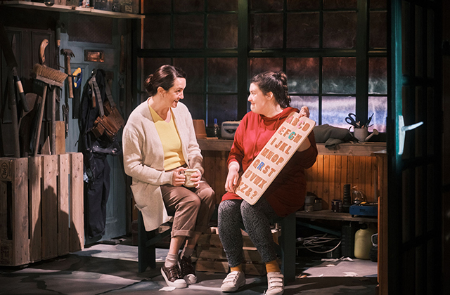 Grace Kiely and Eleanor Walsh, as Mam and Grace, sat down looking at each other fondly. Grace holds a wooden board with the alphabet on it.