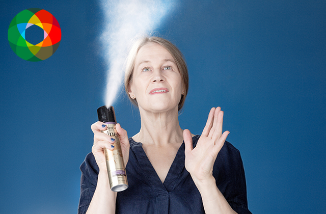 Michelle Read against a blue background, spraying a can of hairspray into the air.