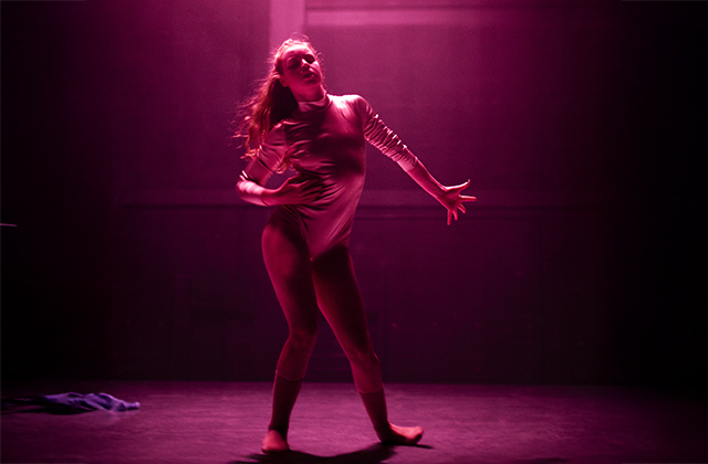 A dancer under dramatic pink lighting, with one arm outstretched.