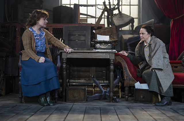 Caitriona and Mary are in character sitting across a table, staring at each other, they appear to be having a difficult conversation. The stage and costume is decorated in early twentieth century attire. Production shots from Outrage by Deirdre Kinahan, photo by Pat Redmond