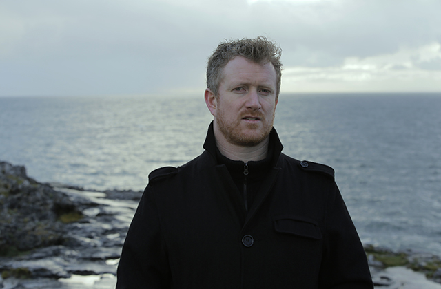 Portrait photo of Padraig Jack in a black coat with the sea in the background