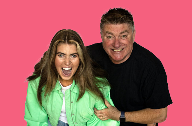 Faye Short and Pat Shortt smiling widely against a bright pink background. Pat is holding Faye's upper arm.