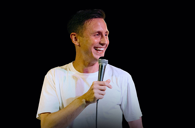 Simple shot of Shane Todd in a white shirt, smiling widely and holding a microphone.