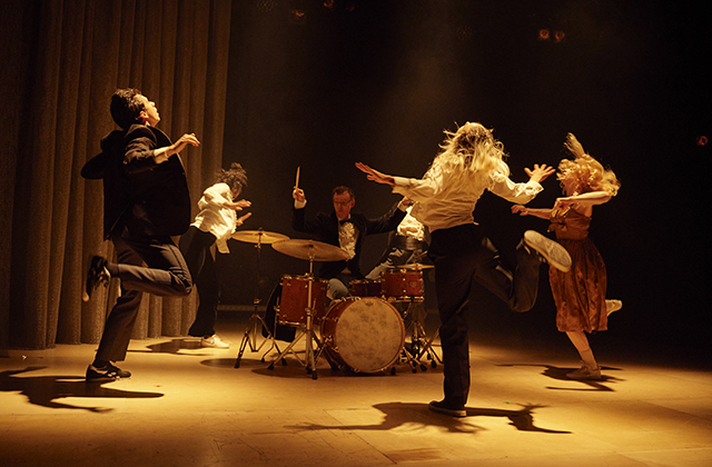 A large group of dancers with arms outstretched and one knee bent, in full motion, with drummer Conor Guilfoyle drumming in the centre.