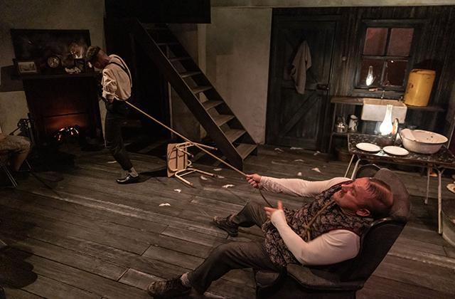 Rory Nolan locked in a tug of war with another man whose face is turned away from the camera. They are in an old Irish sitting room.