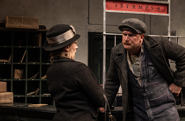 Rory Nolan confronting a woman with her face turned away from the camera. He has a flat cap on and a quizzical look on his face.