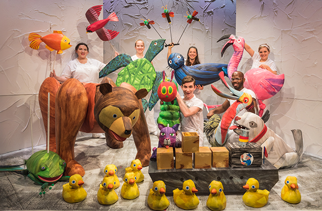 The full cast of The Very Hungry Caterpillar Show, including dozens of colourful puppets - rubber ducks, brown bear, a turtle, birds, fish, a frog, a dog, a cat and the titular caterpillar. Puppet performers smile for the camera.